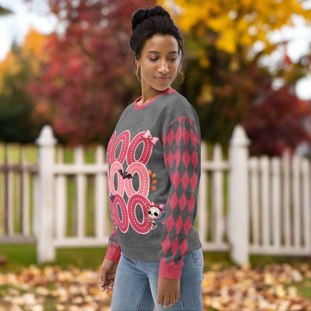 Woman wearing a gray sweater with pink patterns in an outdoor setting with trees and a white fence.