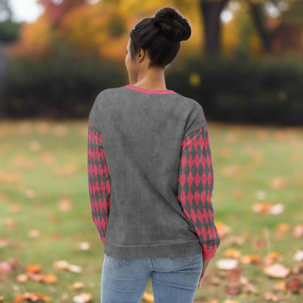Person wearing a gray sweater with pink diamond patterns in an outdoor setting with blurred background