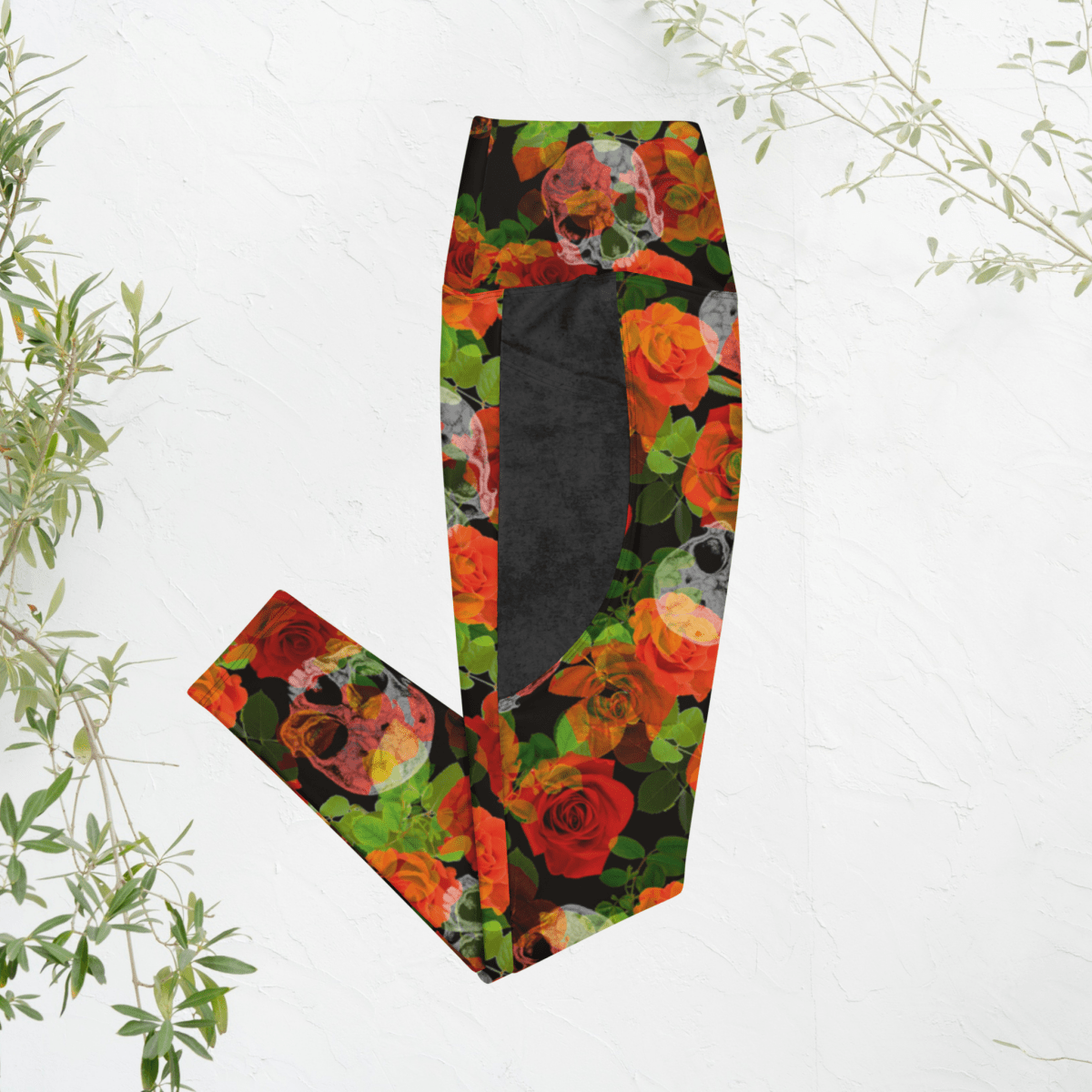 Colorful floral and skull patterned leggings on a white background with green leaves.