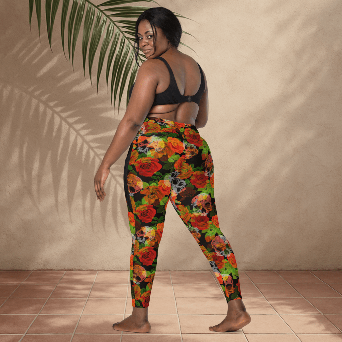 Woman wearing colorful floral sleggings with a beige wall and plant in the backgroundull