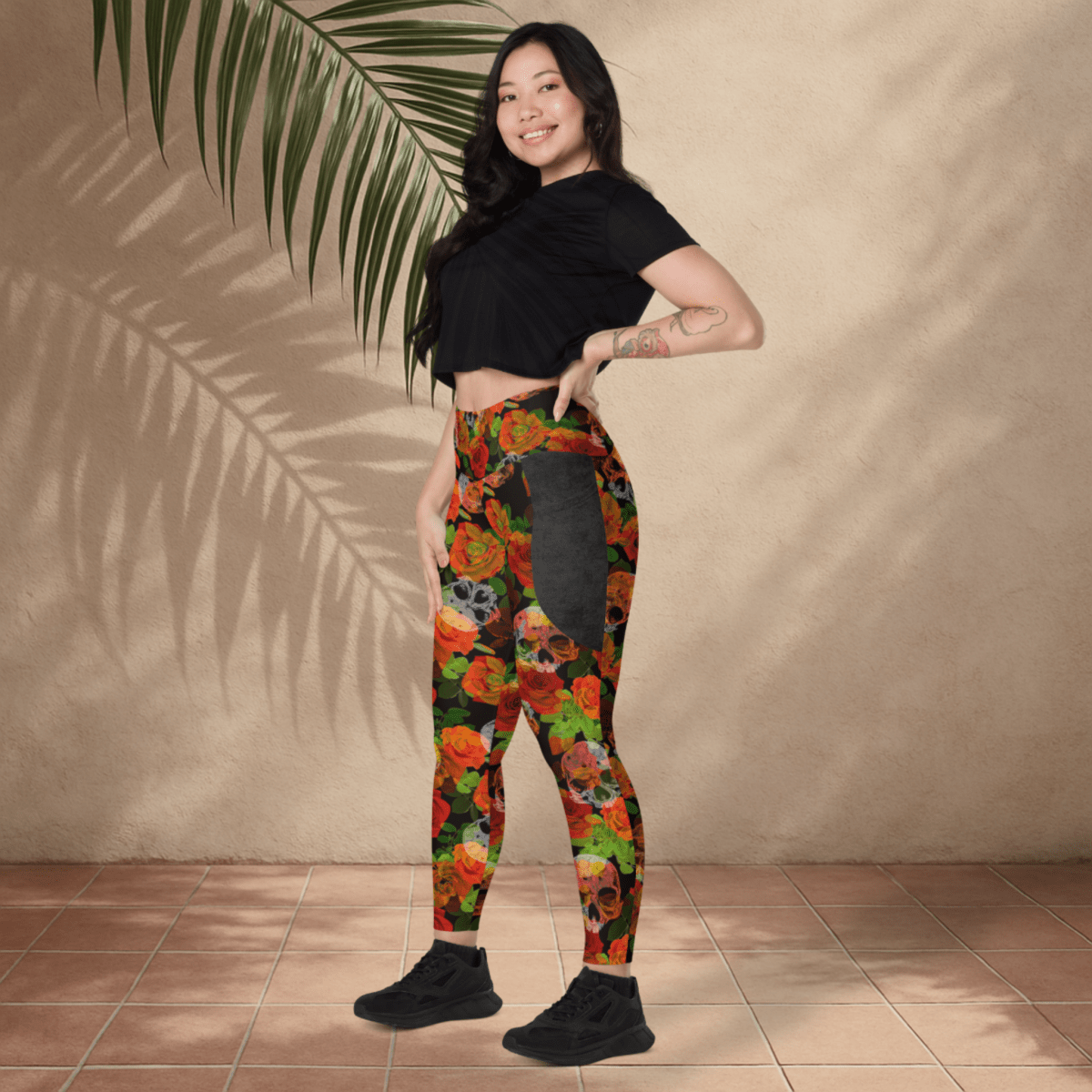 Woman wearing colorful floral skull leggings and a black crop top against a beige wall.