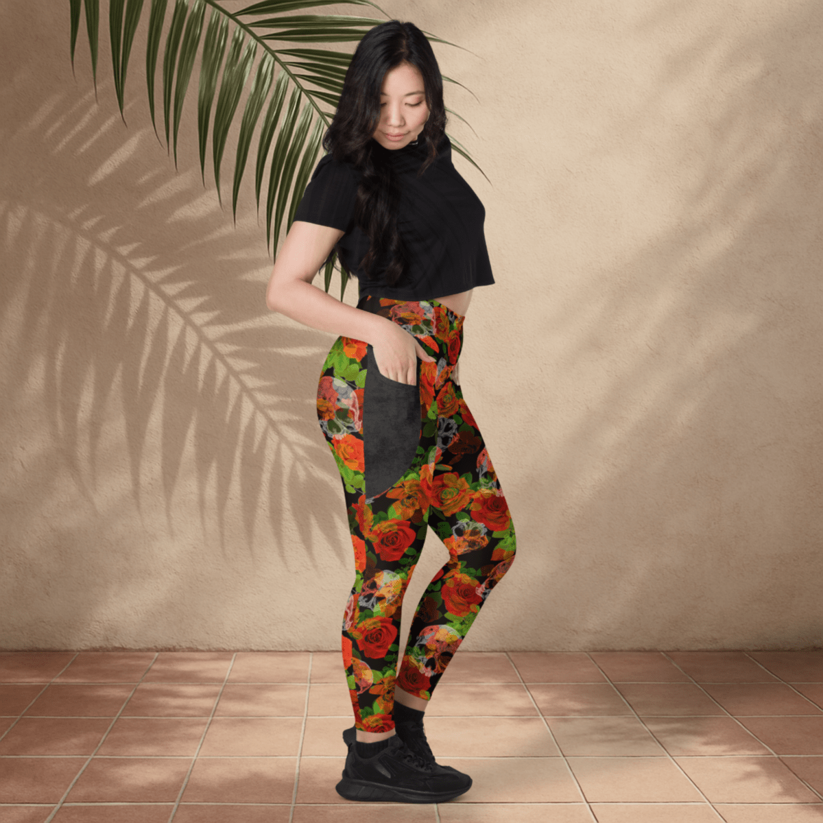 Woman wearing colorful floral skull leggings and a black top against a beige wall.