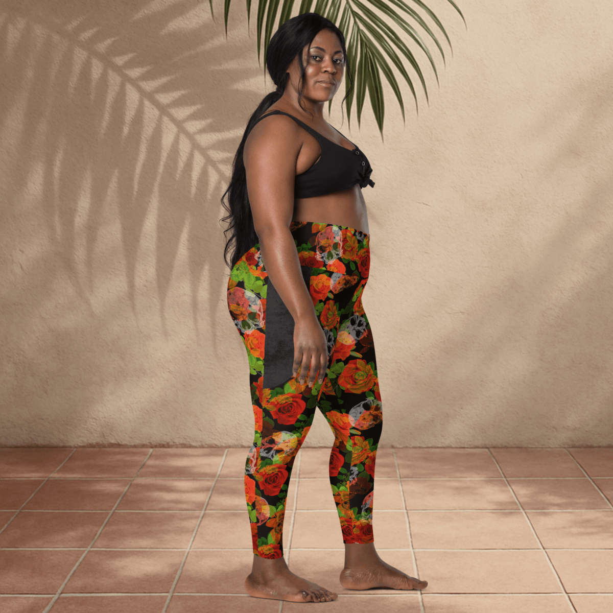 Woman wearing colorful floral skull leggings and a black top against a beige wall.