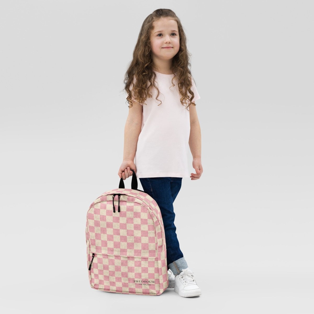 Young girl holding a pink checkered backpack against a plain background