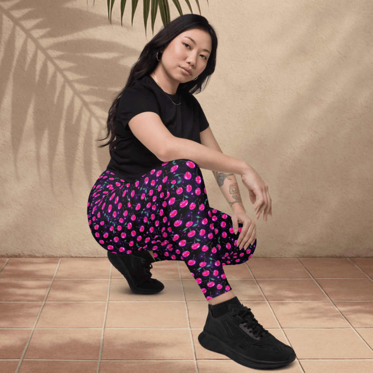 Woman wearing a black t-shirt and pink cherry print pants sitting on a tiled floor.