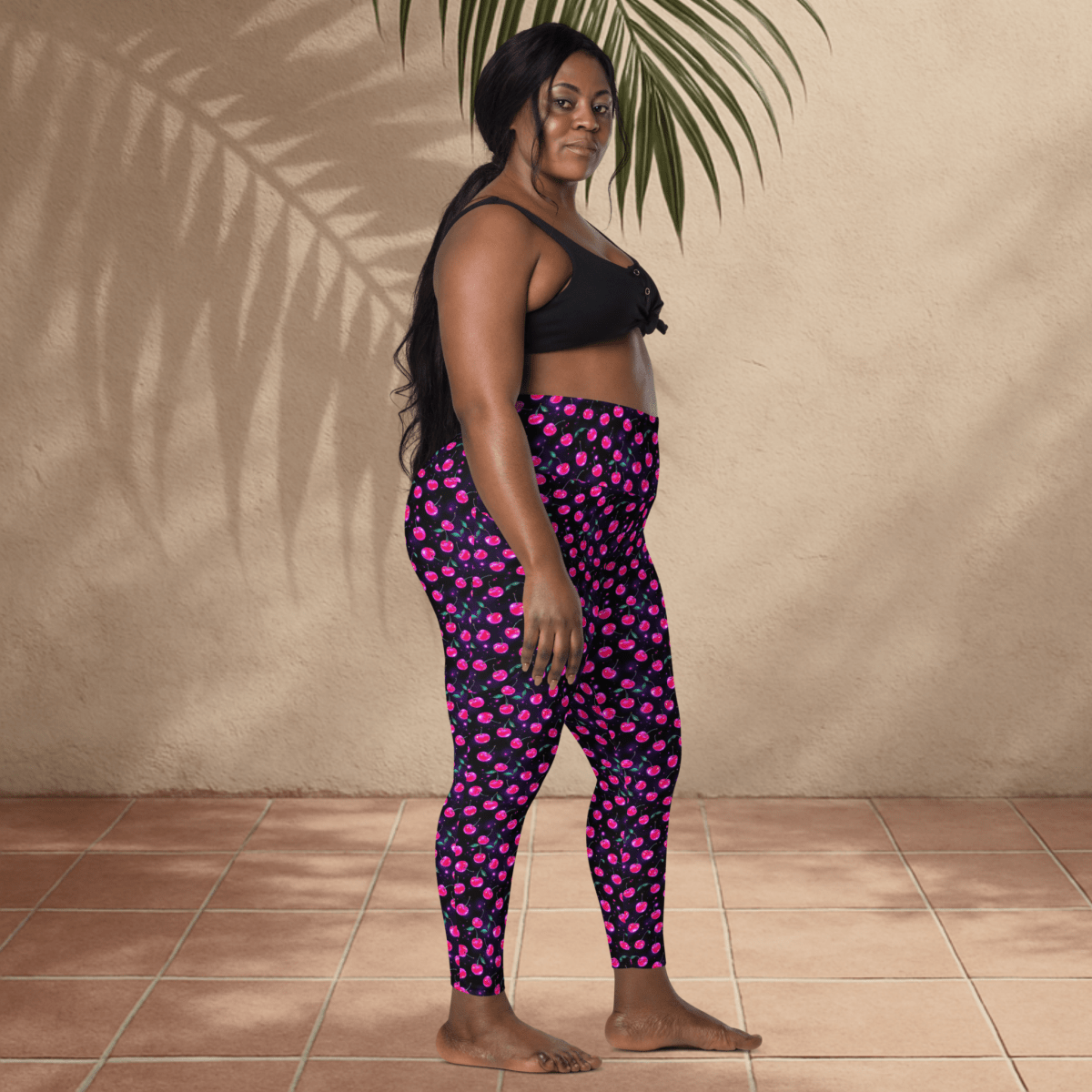 Woman wearing black and pink cherry print patterned leggings against a beige wall.