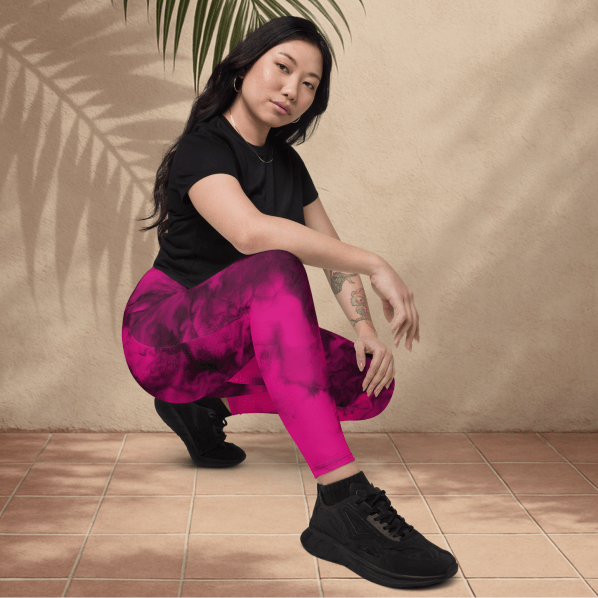 Woman in black top and pink leggings sitting on a tiled floor with a beige wall and plant in the background