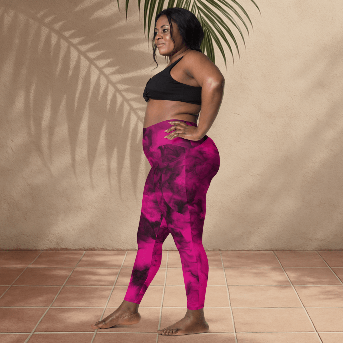 Woman wearing pink and black patterned leggings and black sports bra against a beige wall.