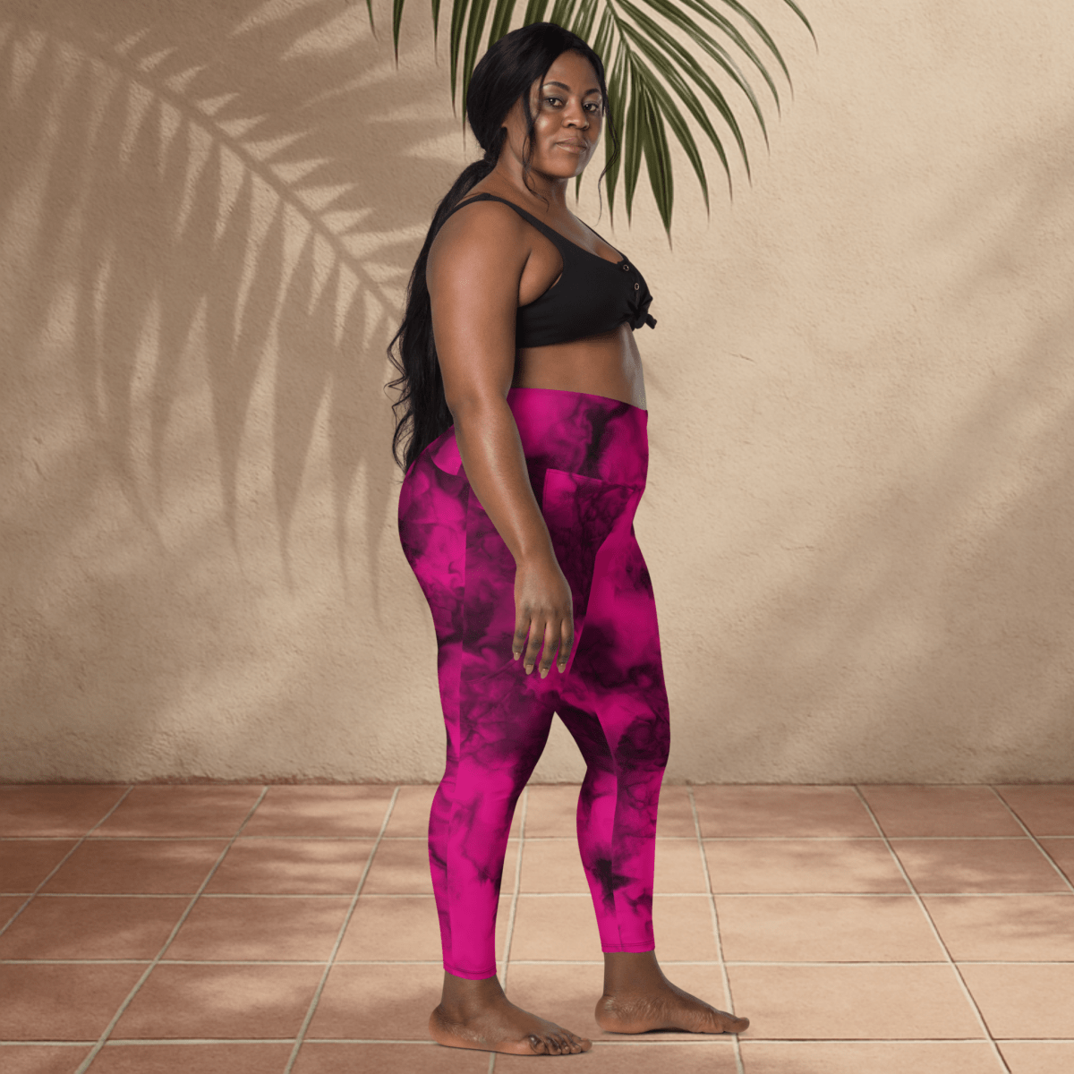 Woman wearing pink tie-dye leggings and black top standing against a beige wall.