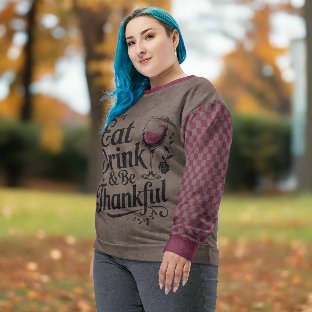 Woman wearing a sweater with 'Eat Drink & Be Thankful' text and wine glass design outdoors