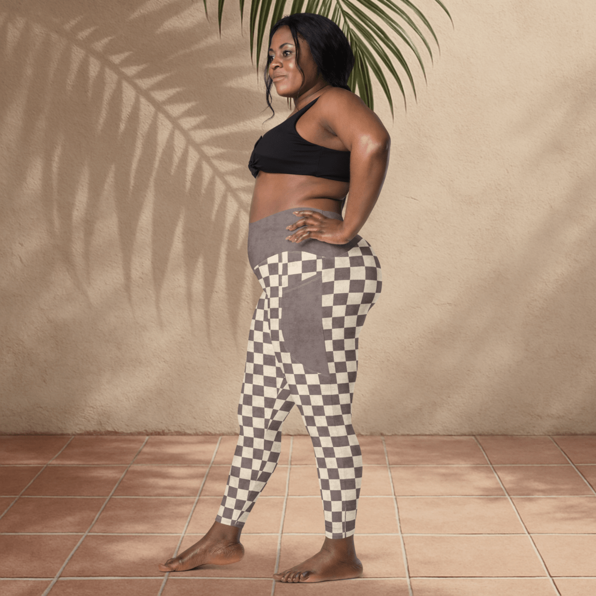 Woman wearing black sports bra and checkered leggings standing against a beige wall.