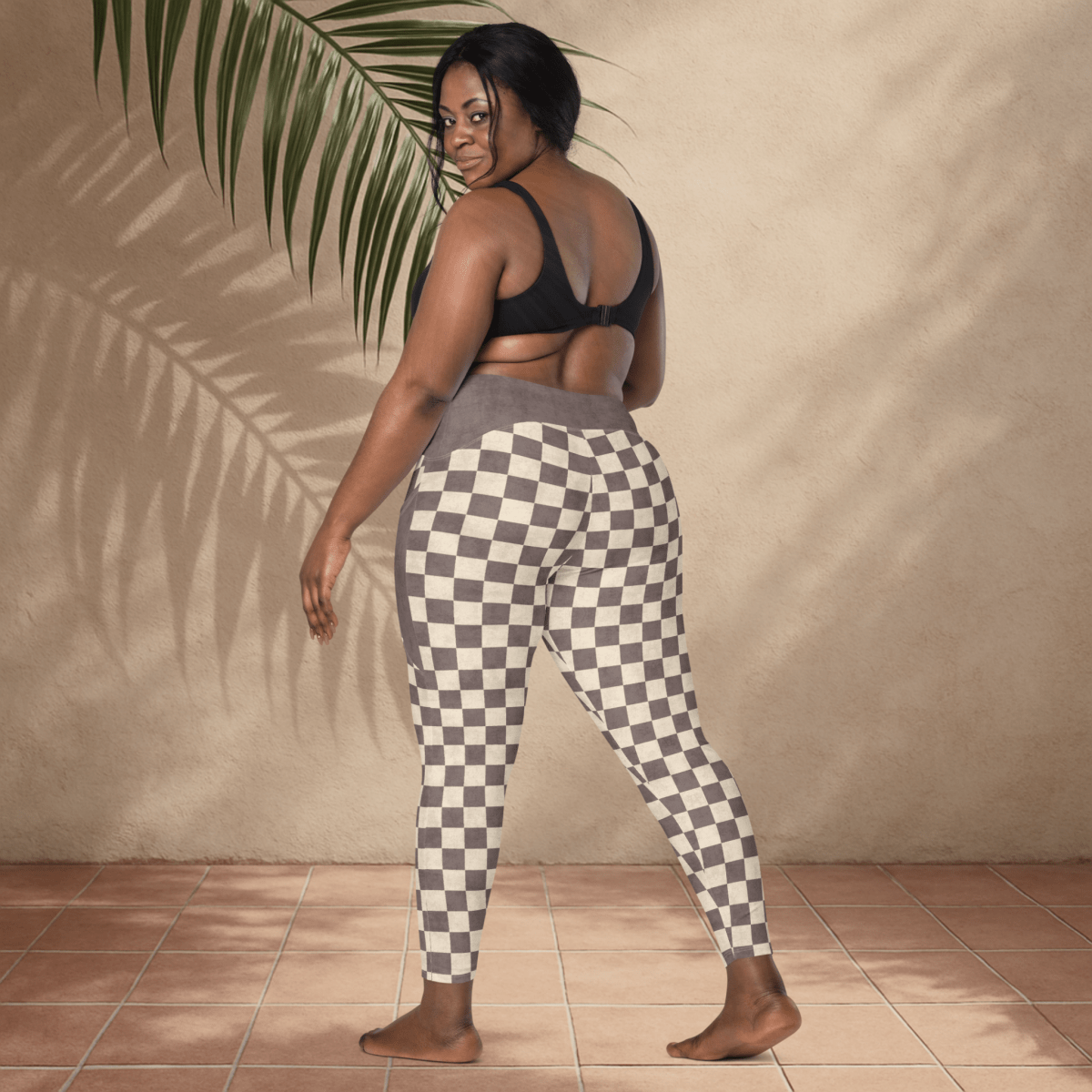 Woman wearing checkered pants and a black top against a beige wall.