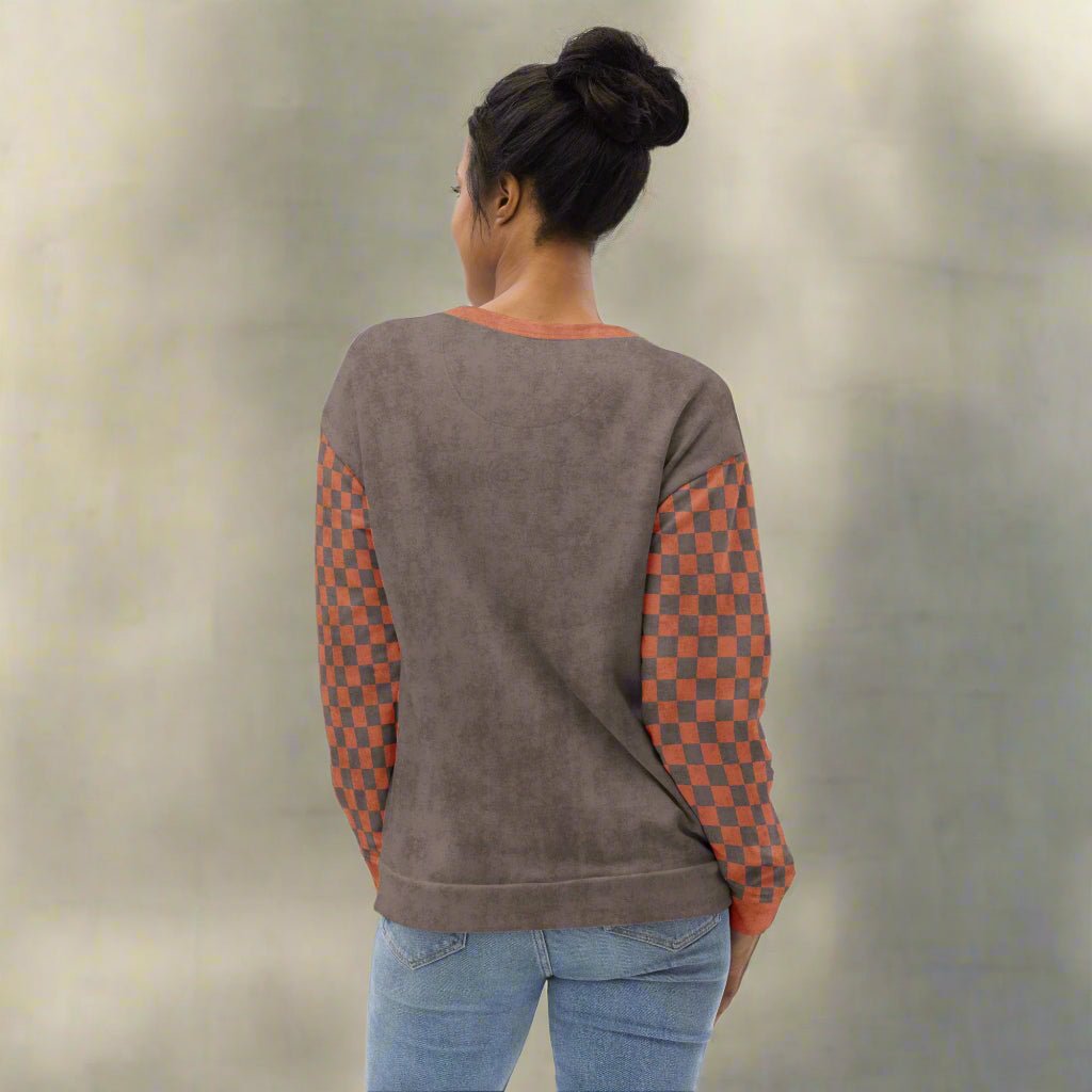 Person wearing a brown sweatshirt with checkered sleeves against a neutral background