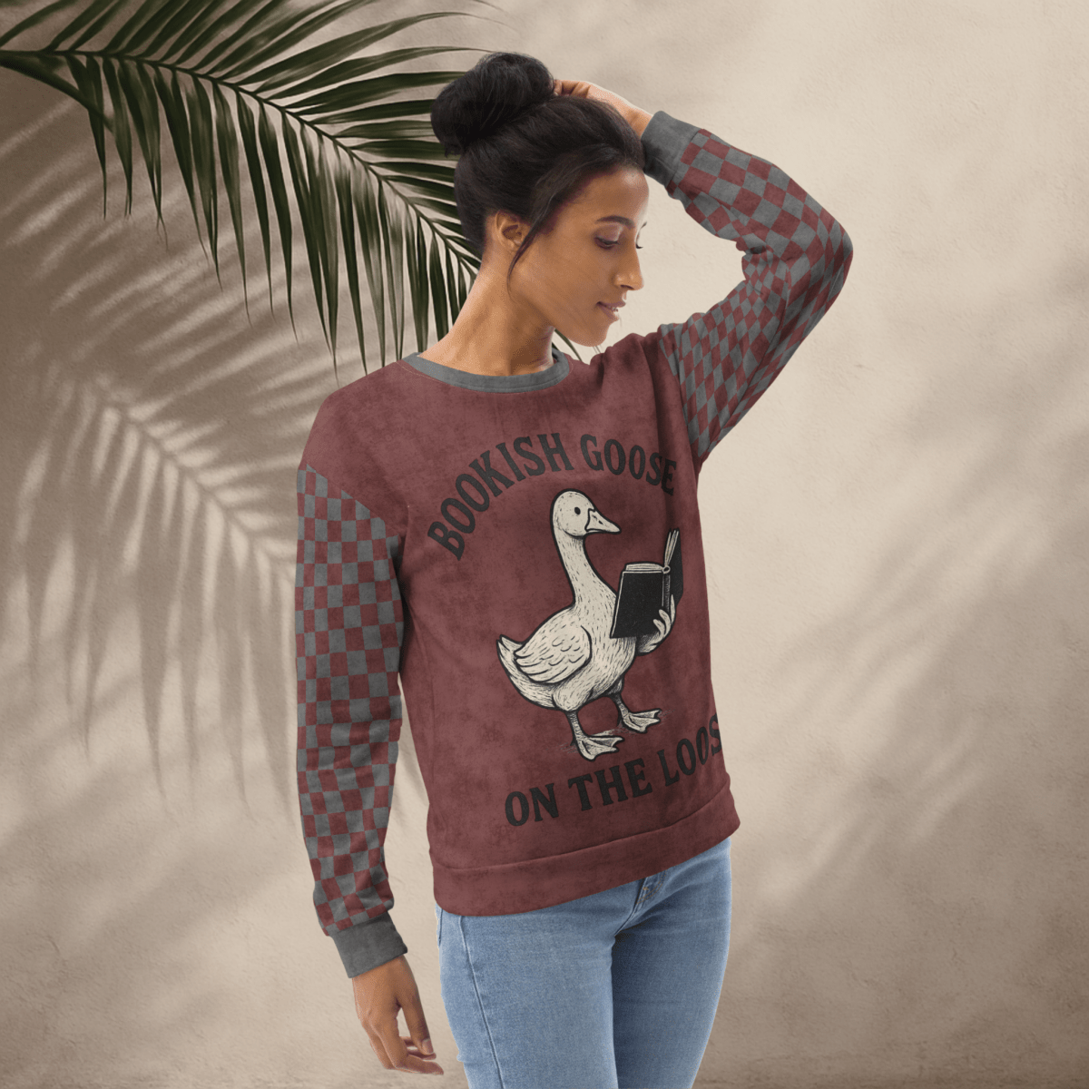 Woman wearing a sweatshirt with a goose graphic and text, standing against a neutral background with a leaf.