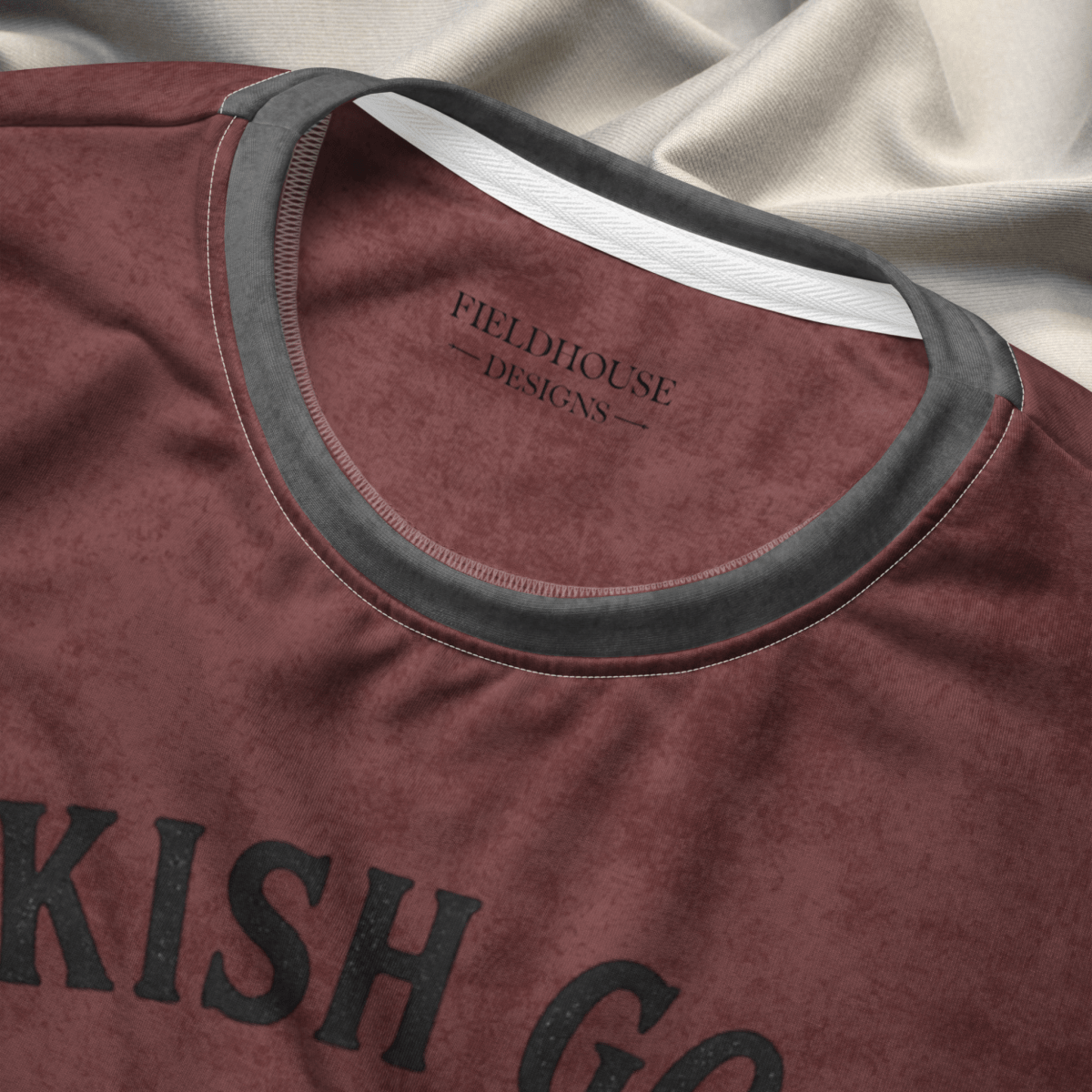 burgundy shirt with 'Fieldhouse Designs' branding and text on a beige fabric background