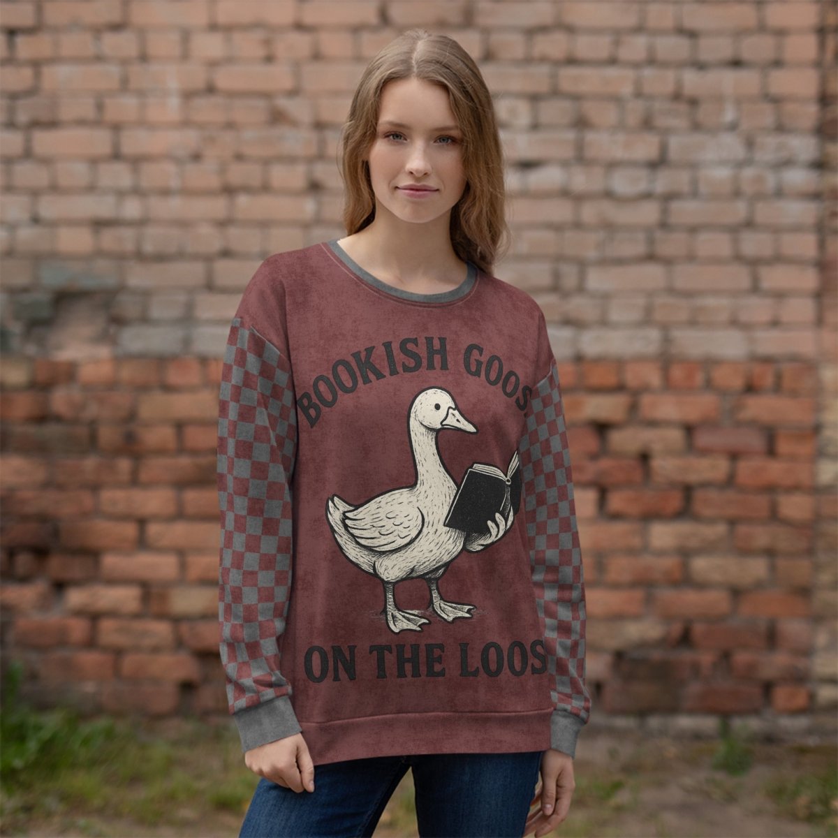 Person wearing a burgundy sweater with a goose graphic and text, standing against a brick wall.
