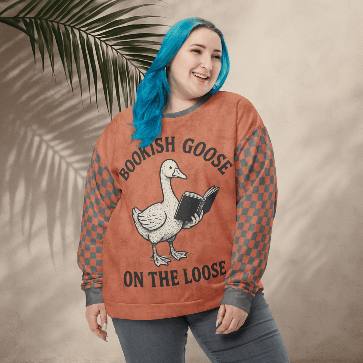 Person wearing a sweater with a goose reading graphic and text 'Bookish Goose on the Loose", standing against a beige wall with a leafy branch.