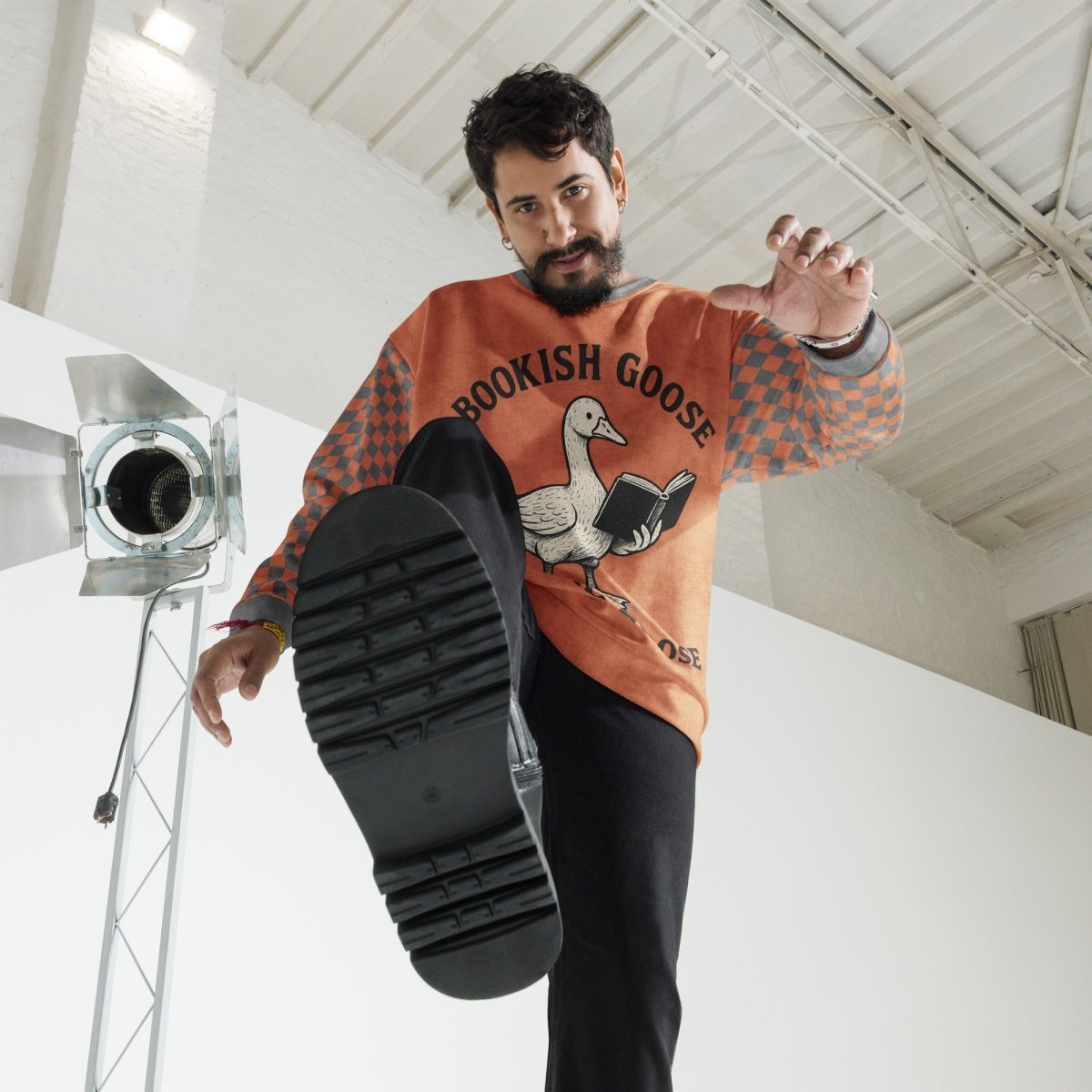 Man wearing a sweater with a graphic design, holding up a black shoe sole indoors.