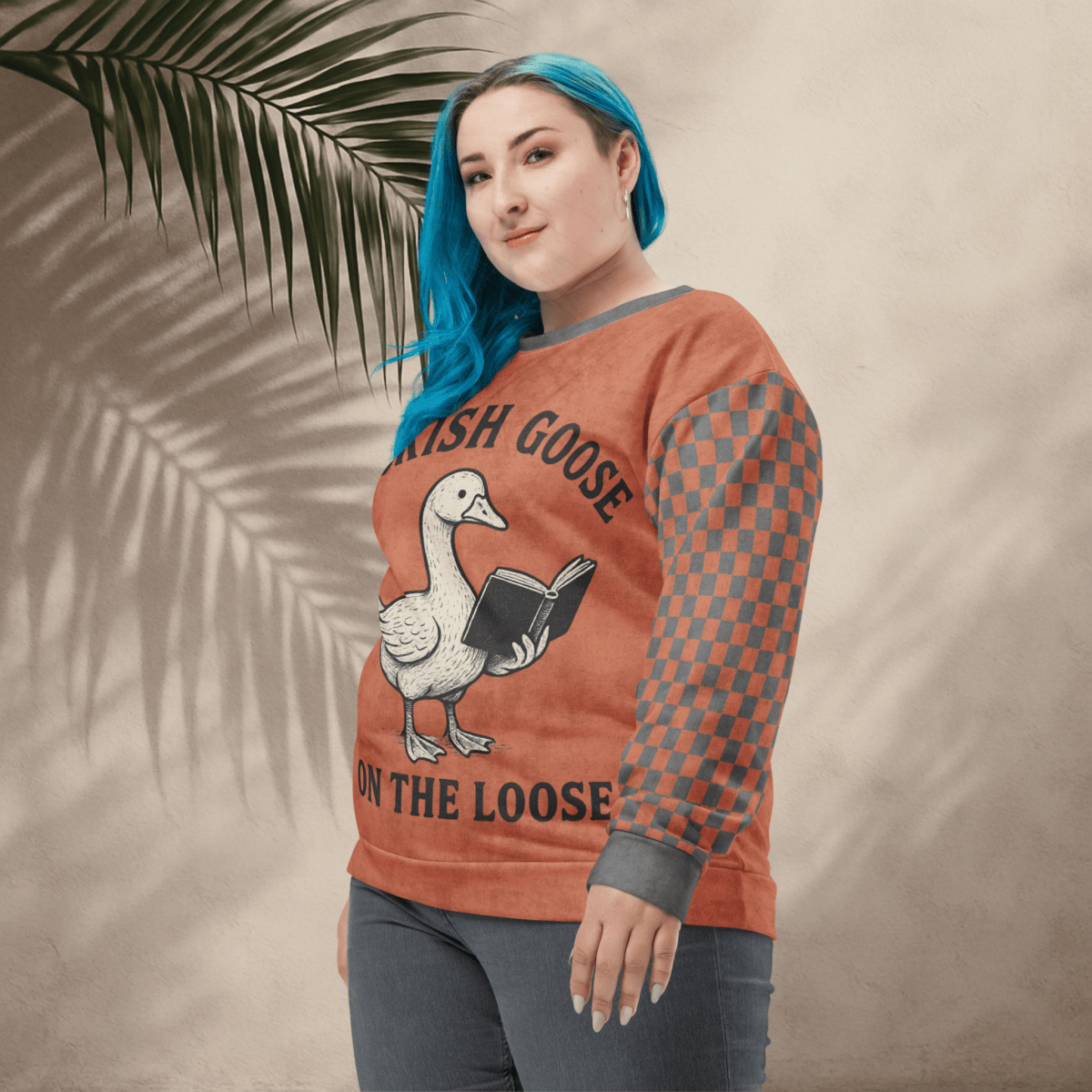 Person wearing a sweater with a goose reading a book design and text 'Bookish Goose on the Loose', standing against a beige wall with a leafy branch.
