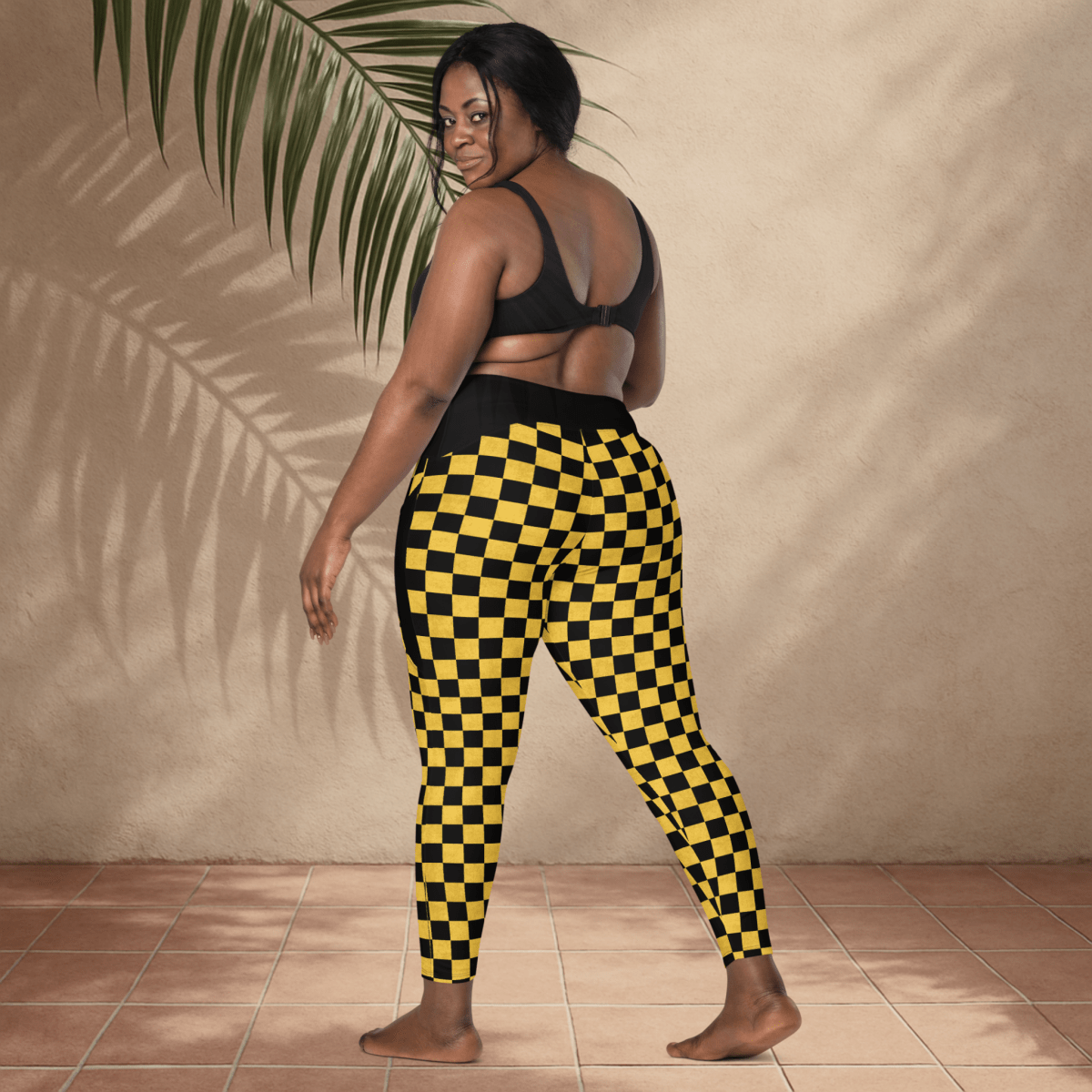 Person wearing black and yellow checkered pants standing against a beige wall.