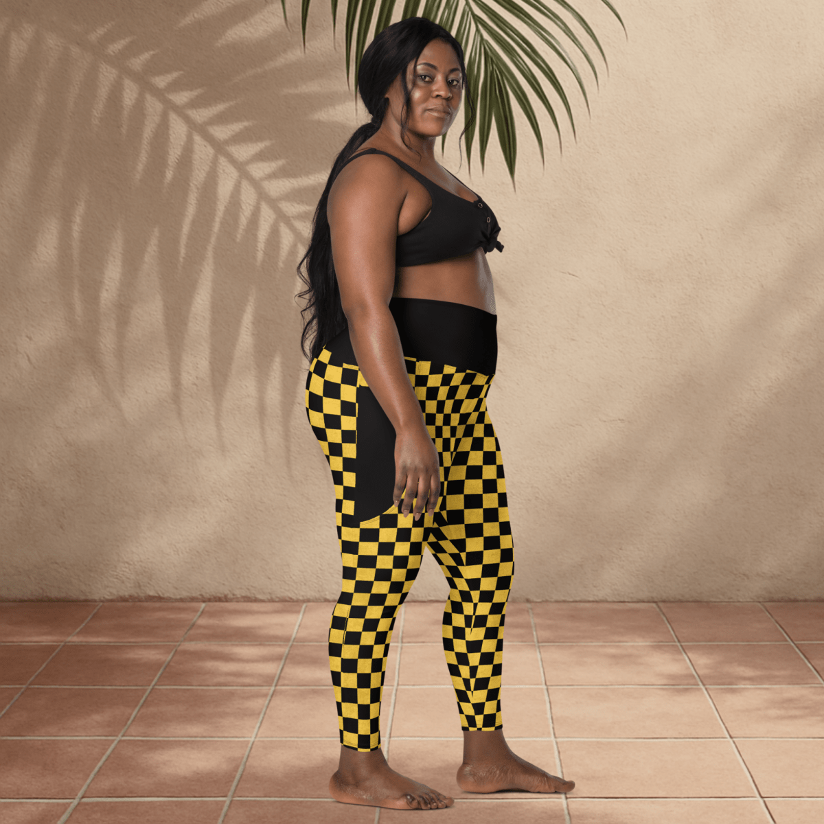 Woman wearing black and yellow checkered pants standing against a beige wall.