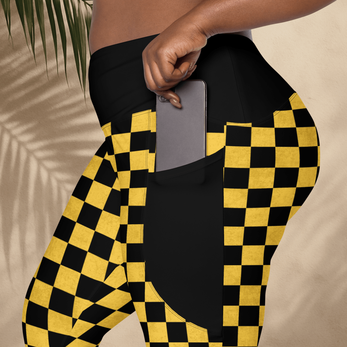 Person wearing black and yellow checkered pants with a phone in the pocket against a beige background.