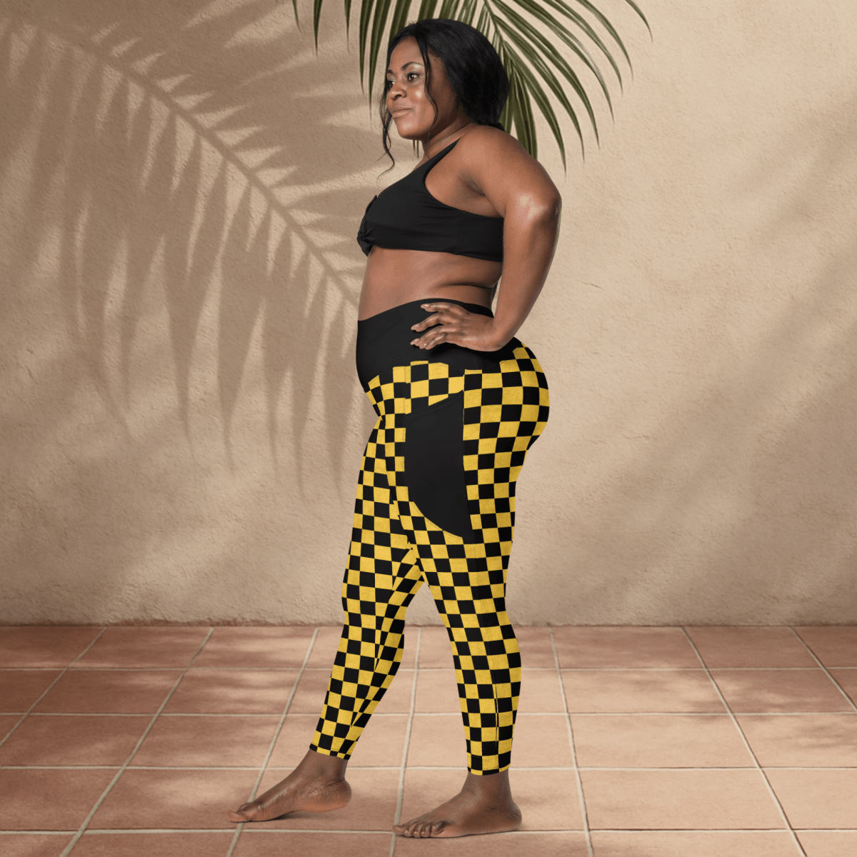 Woman wearing black and yellow checkered leggings and black sports bra against a beige wall.