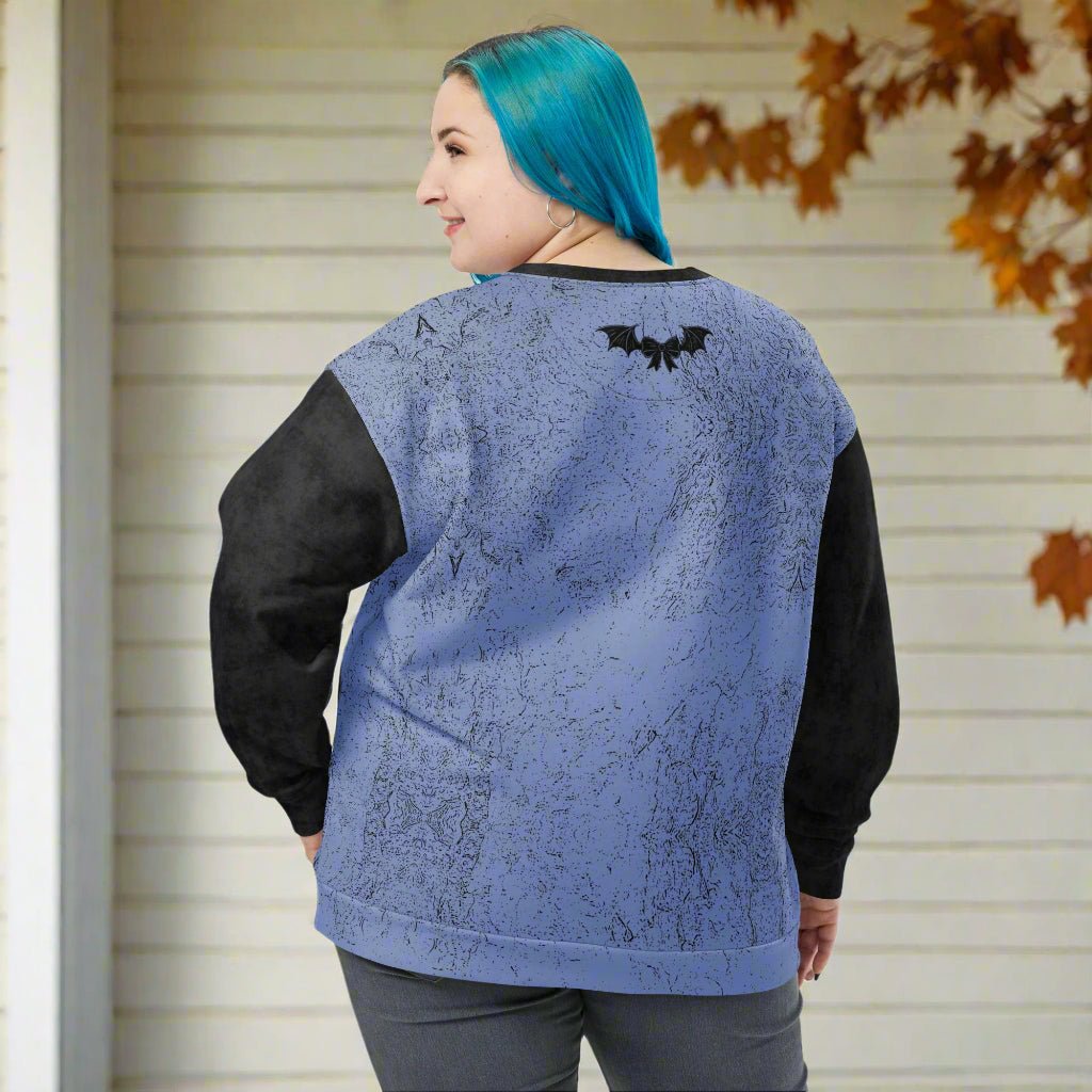 Person wearing a blue and black sweater with a bat design on the back, standing in front of a beige wall with autumn leaves.