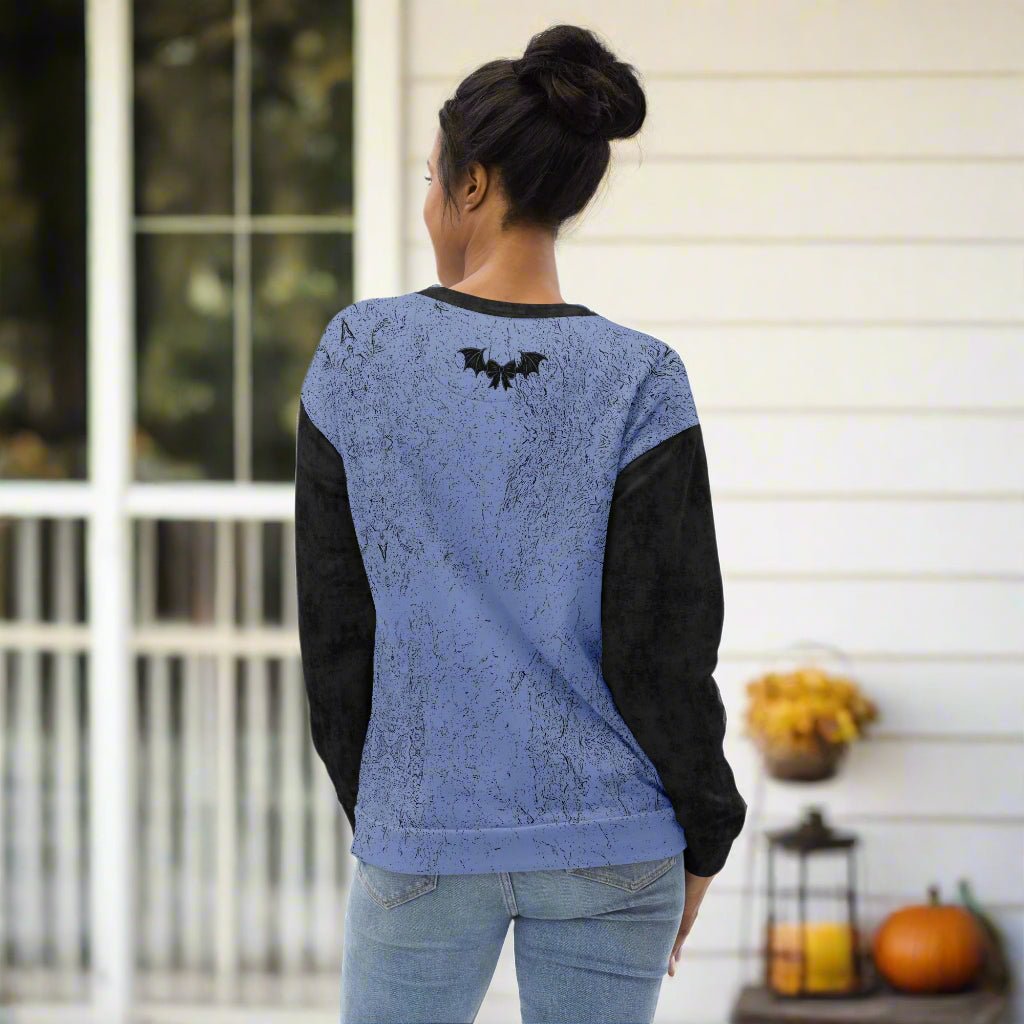 Person wearing a blue and black sweatshirt with a bat design on the back, standing in front of a window.