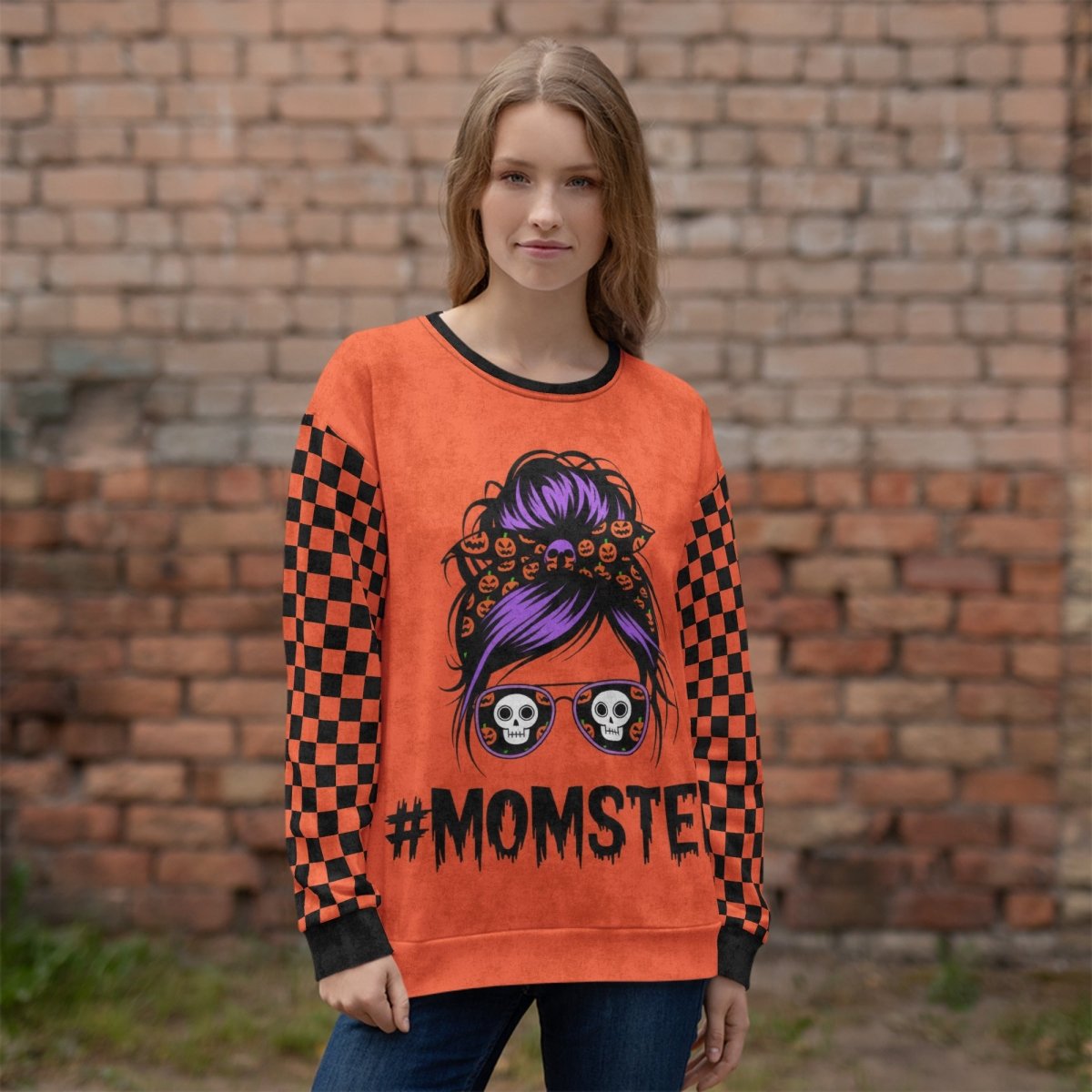 Person wearing an orange sweatshirt with a momster design in front of a brick wall
