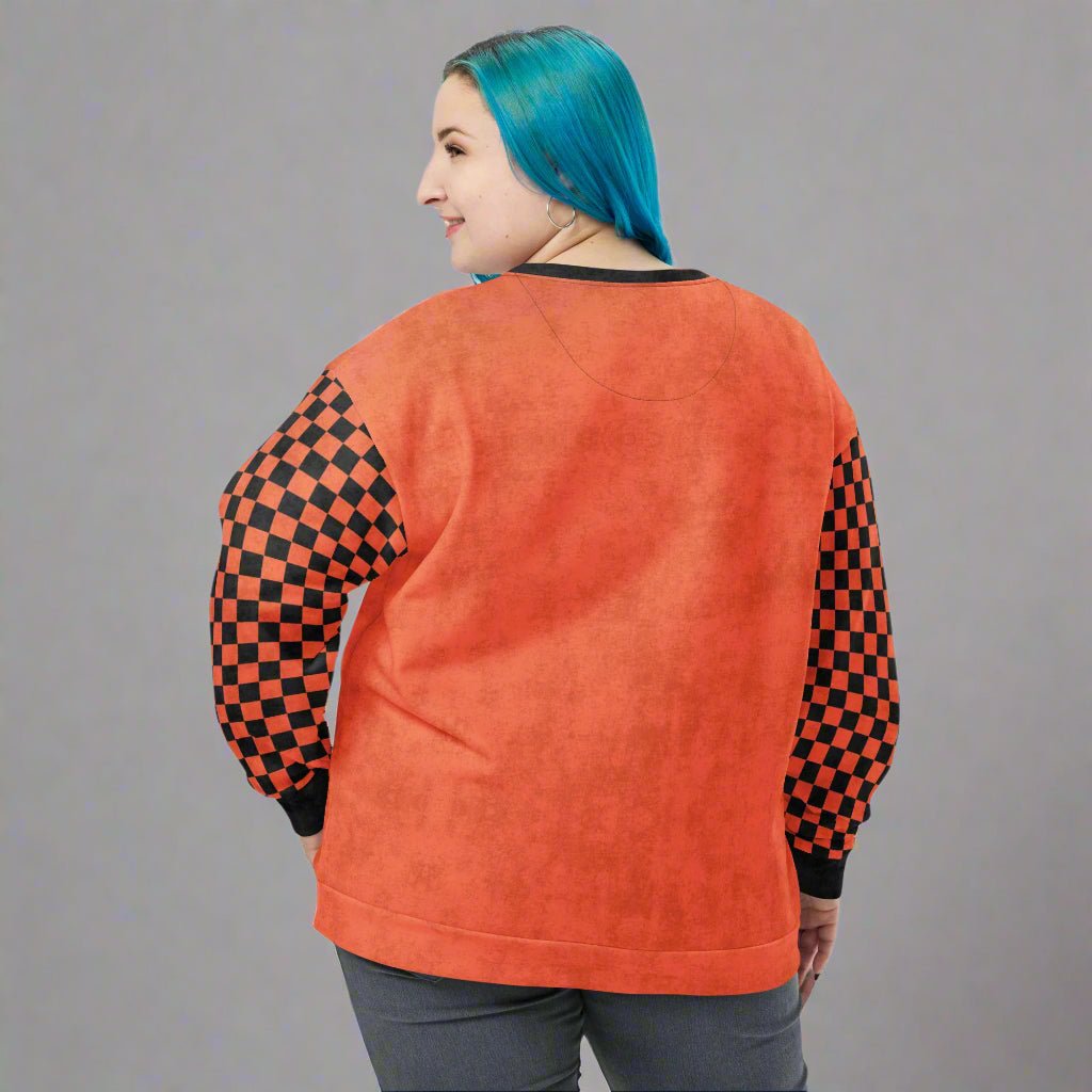 Person wearing an orange sweatshirt with checkered sleeves on a neutral background