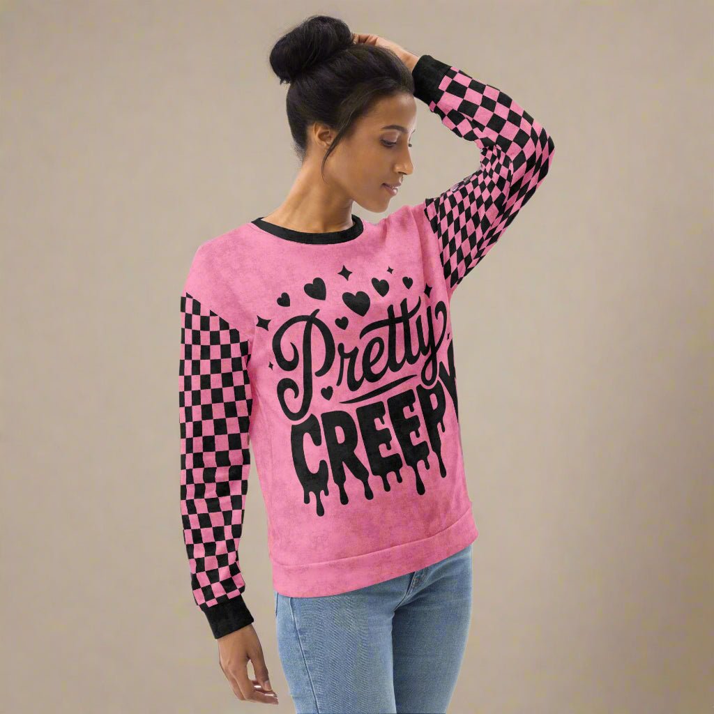 Person wearing a pink sweater with 'Pretty Creepy' text and checkered sleeves on a beige background