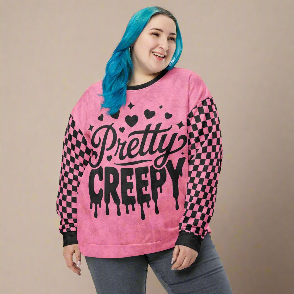 Person wearing a pink sweatshirt with 'Pretty Creepy' text and checkered sleeves on a neutral background