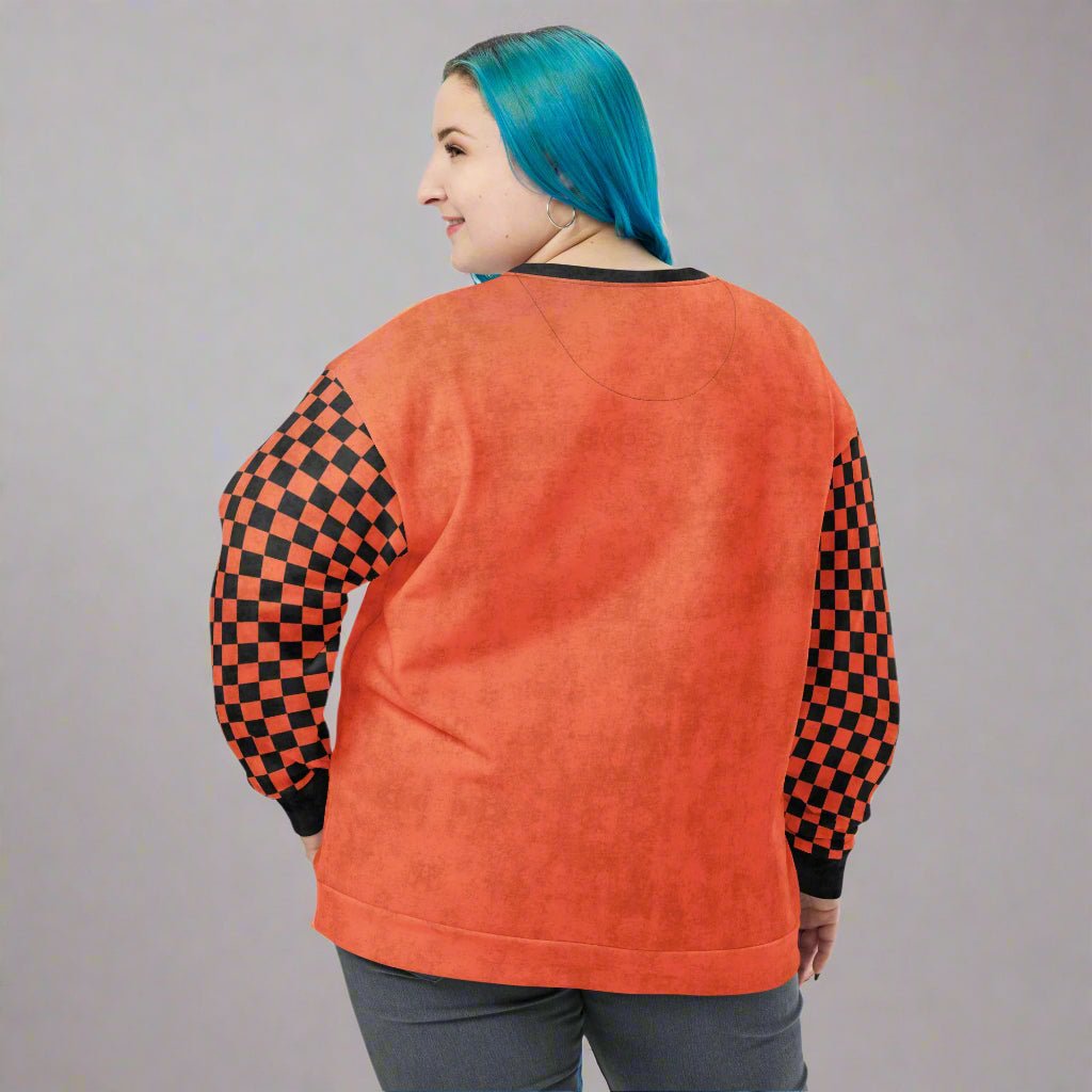 Person wearing an orange sweatshirt with checkered sleeves on a neutral background