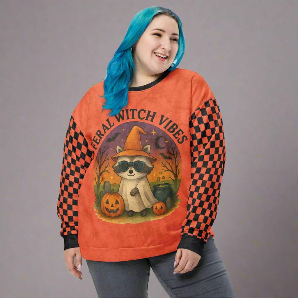Person wearing an orange sweatshirt with a raccoon graphic and 'Feral Witch Vibes' text on a gray background