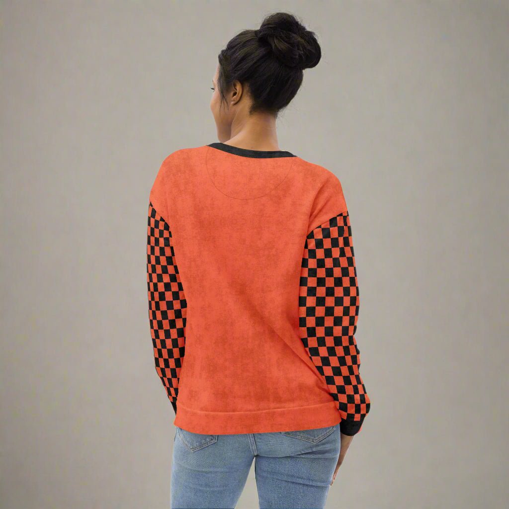 Person wearing an orange sweatshirt with checkered sleeves on a neutral background
