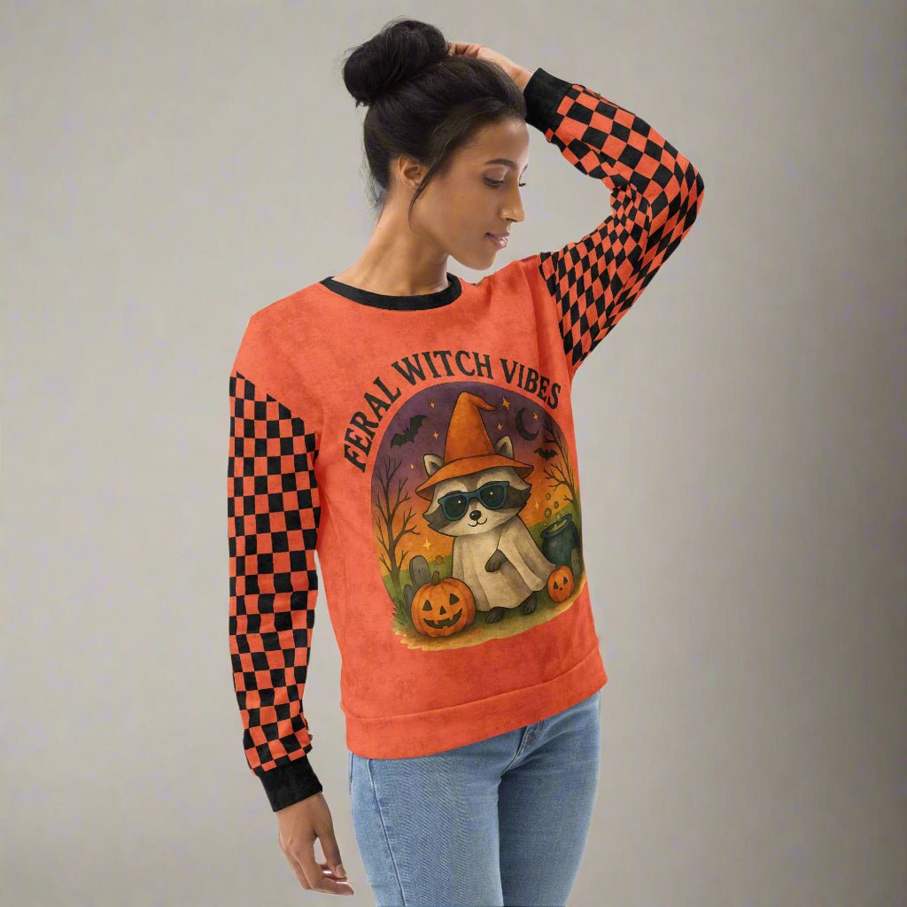 Woman wearing a Halloween-themed sweatshirt with a raccoon graphic and 'Feral Witch Vibes' text.