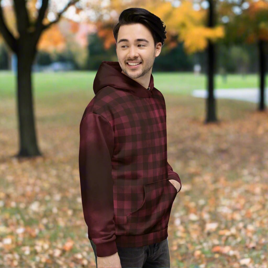 Person wearing a burgundy plaid hoodie in an outdoor setting with trees and fallen leaves.
