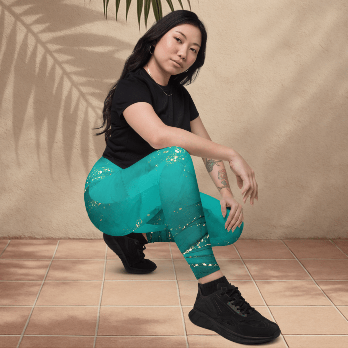 Woman wearing teal leggings with gold patterns and black shoes on a beige background