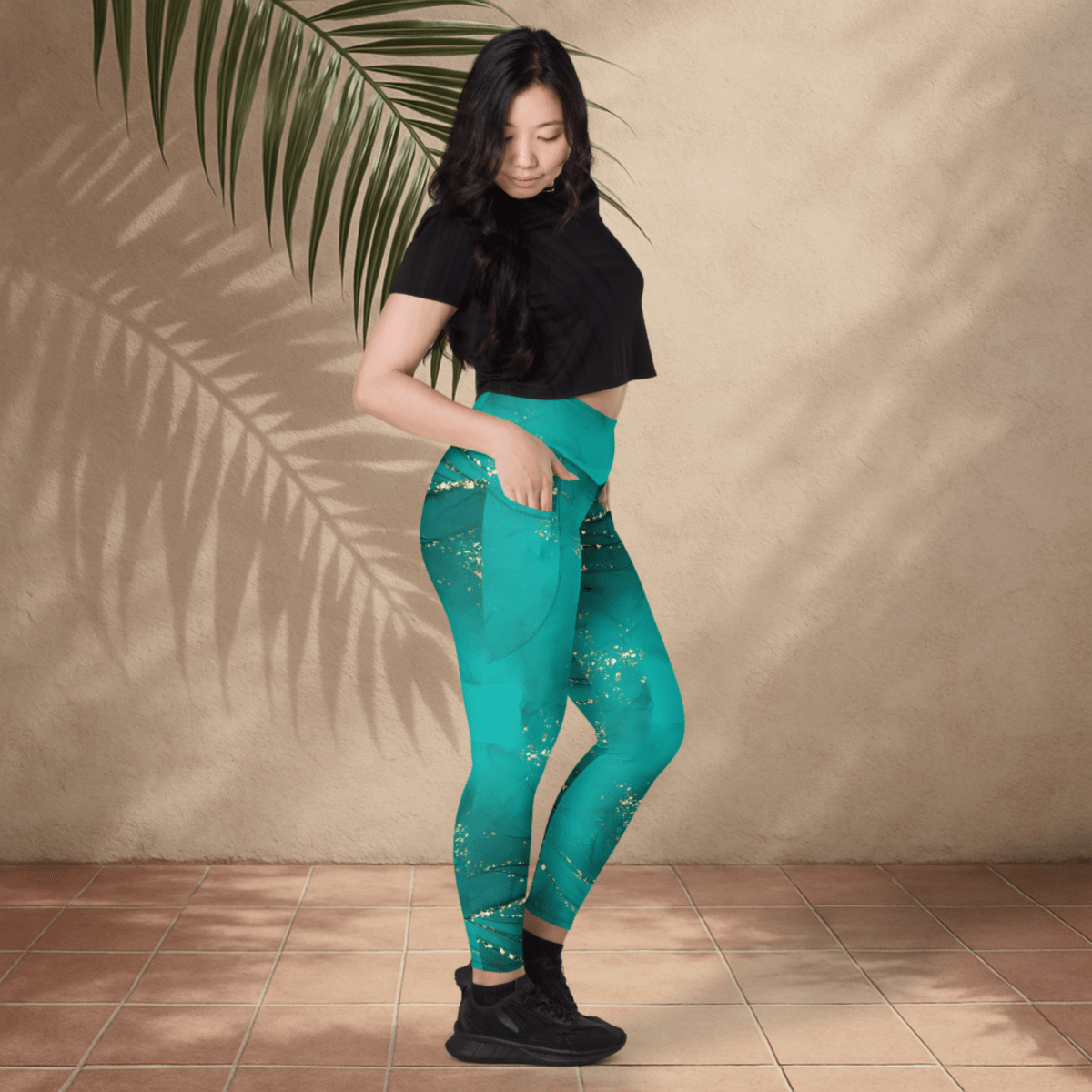 Woman wearing teal leggings with a black top against a beige wall.