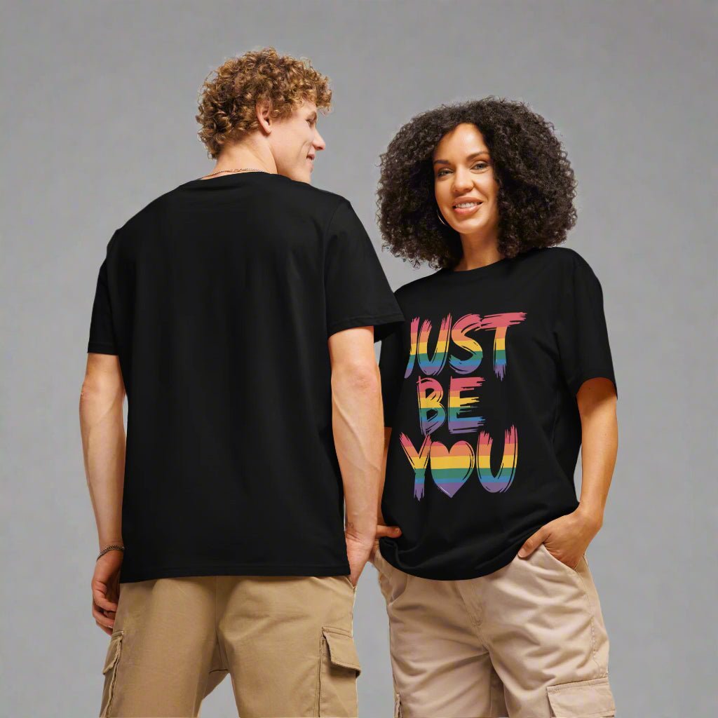 Two people wearing black t-shirts with 'Just Be You' text in colorful letters on a plain background