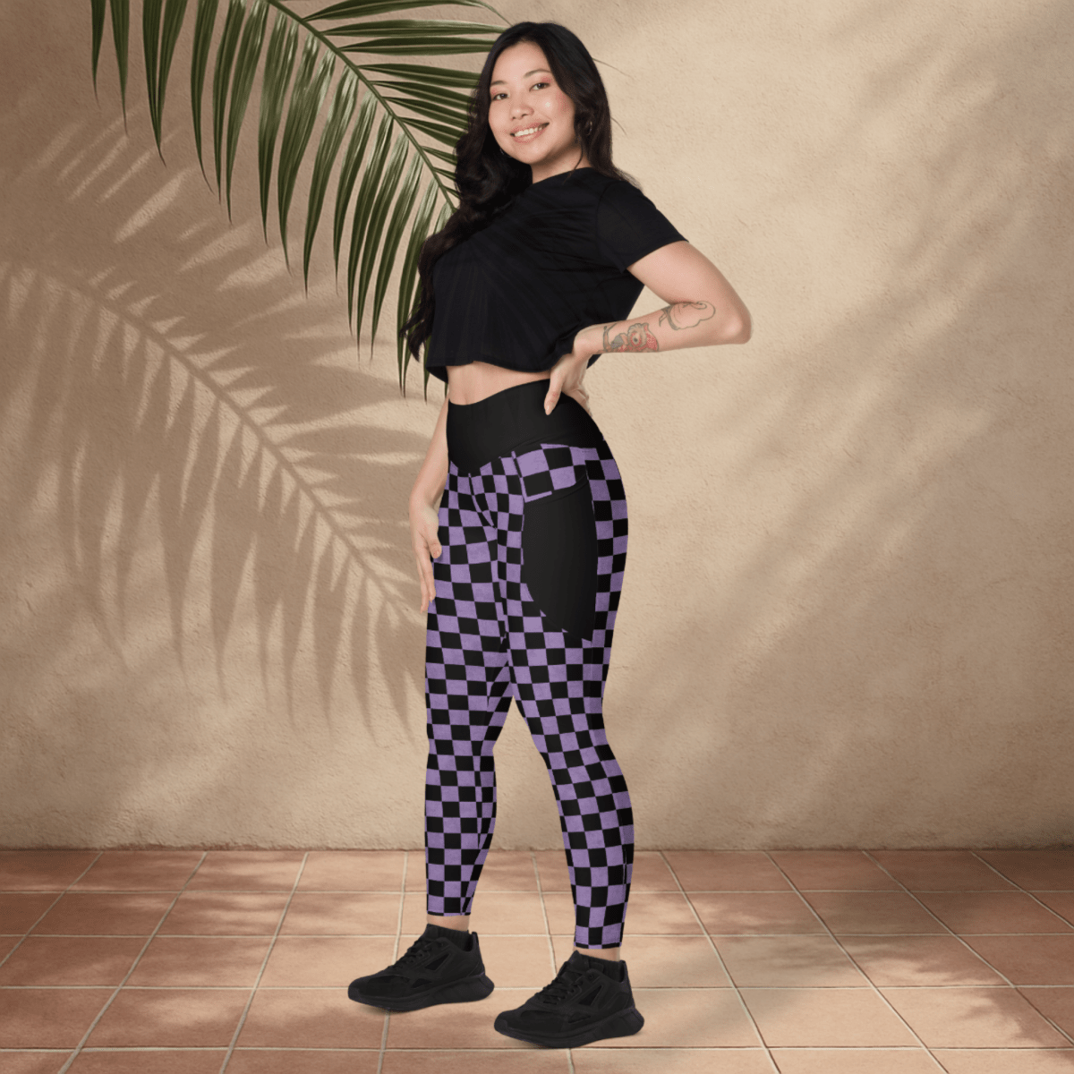 Woman wearing black and purple checkered leggings with a black crop top against a beige wall.
