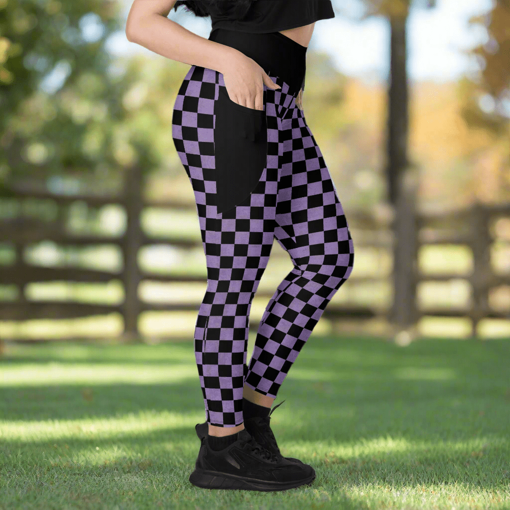 Person wearing black and purple checkered leggings outdoors on a grassy area with a blurred wooden fence in the background.