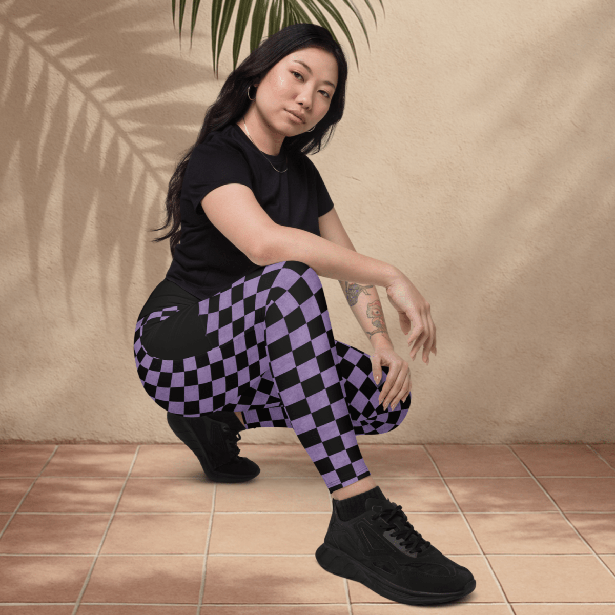 Person wearing a black t-shirt and purple checkered pants sitting on the floor with a plant in the background.