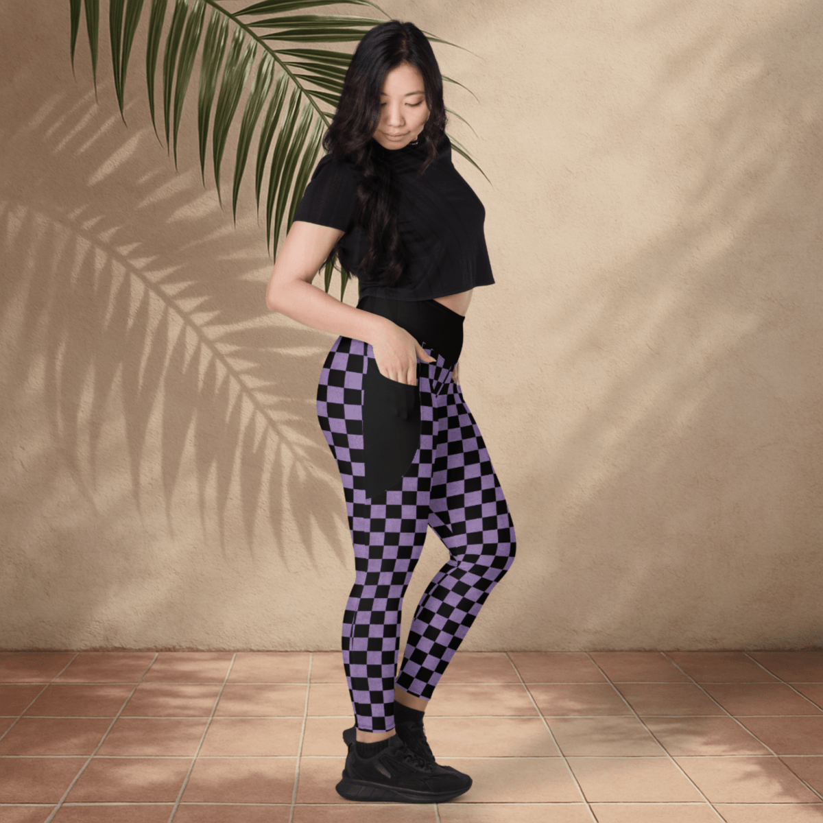 Woman wearing black and purple checkered pants against a beige wall.
