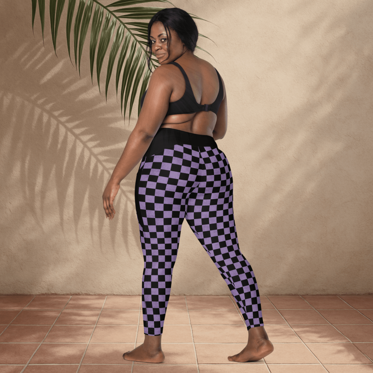 Person wearing black and purple checkered leggings against a beige wall.