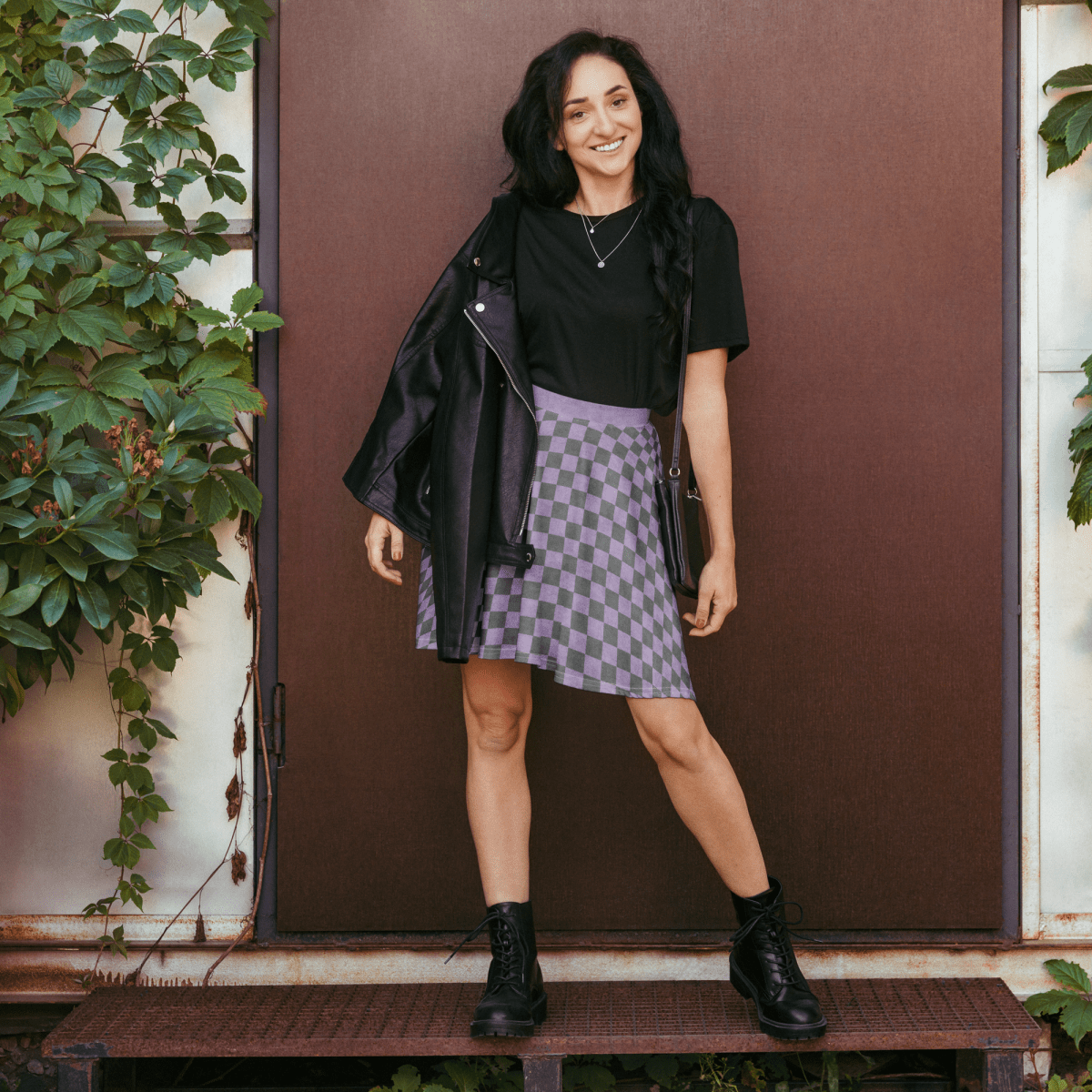 Woman wearing lavender and gray skirt outdoors with a brown door and greenery in the background