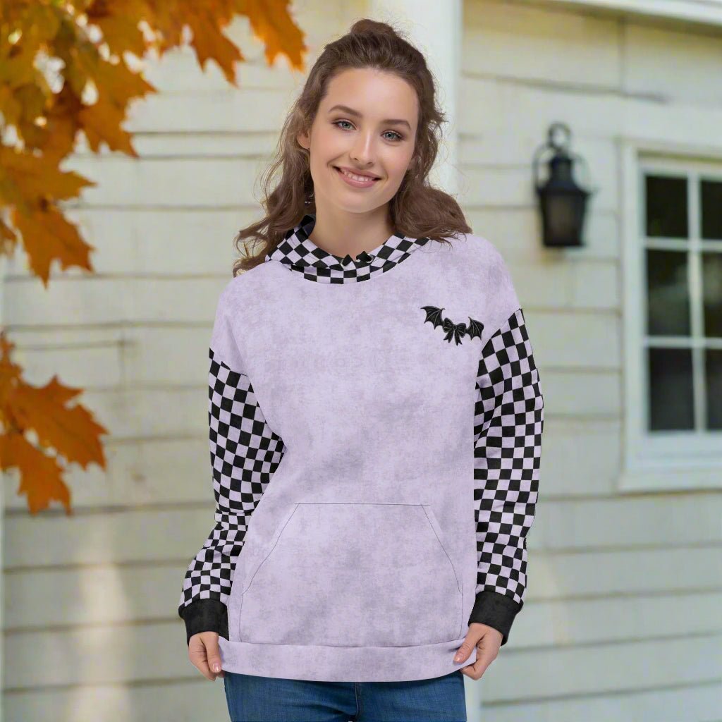 Woman wearing a light purple hoodie with checkered sleeves in front of a house with autumn leaves.