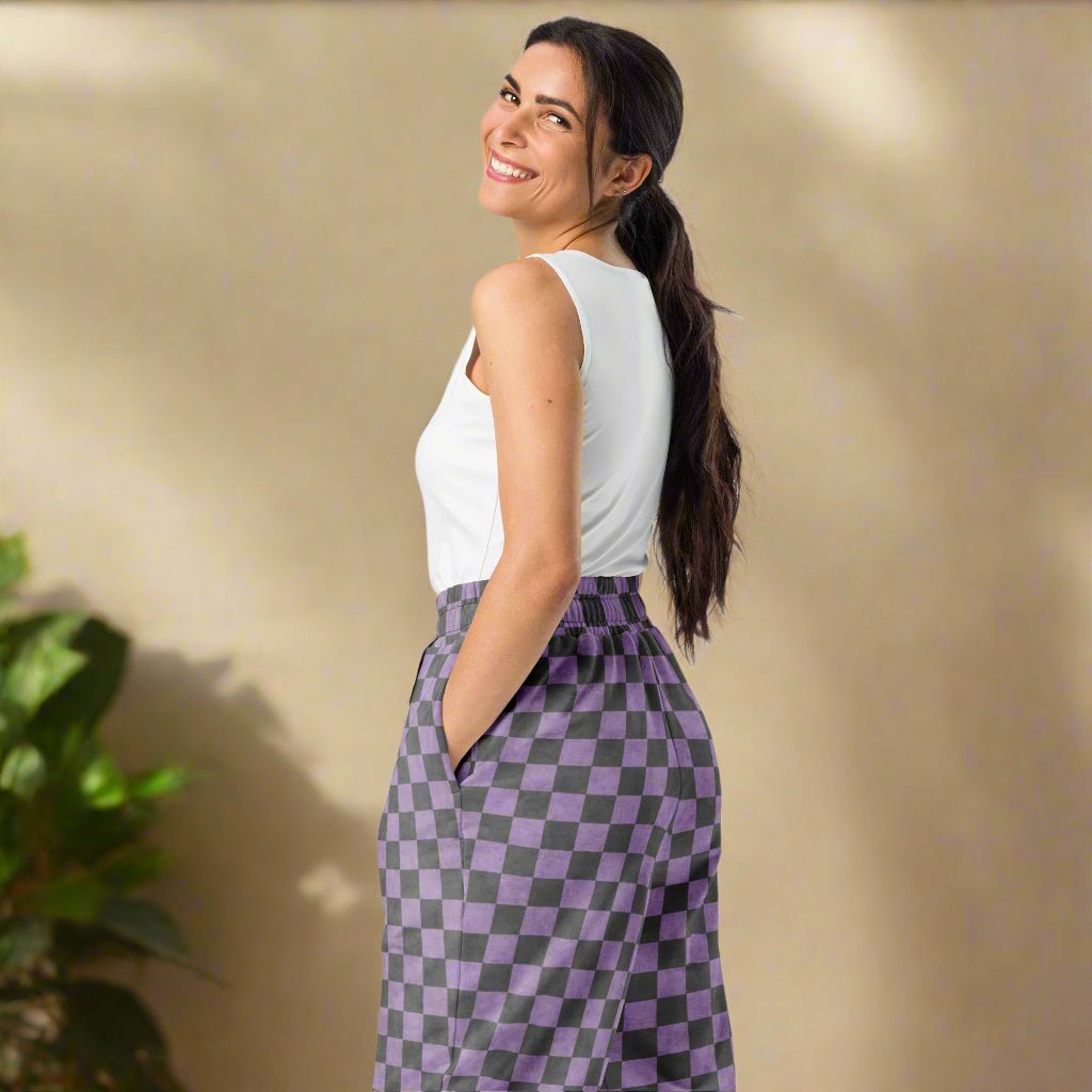 Woman wearing a white sleeveless top and purple checkered pants against a beige wall.