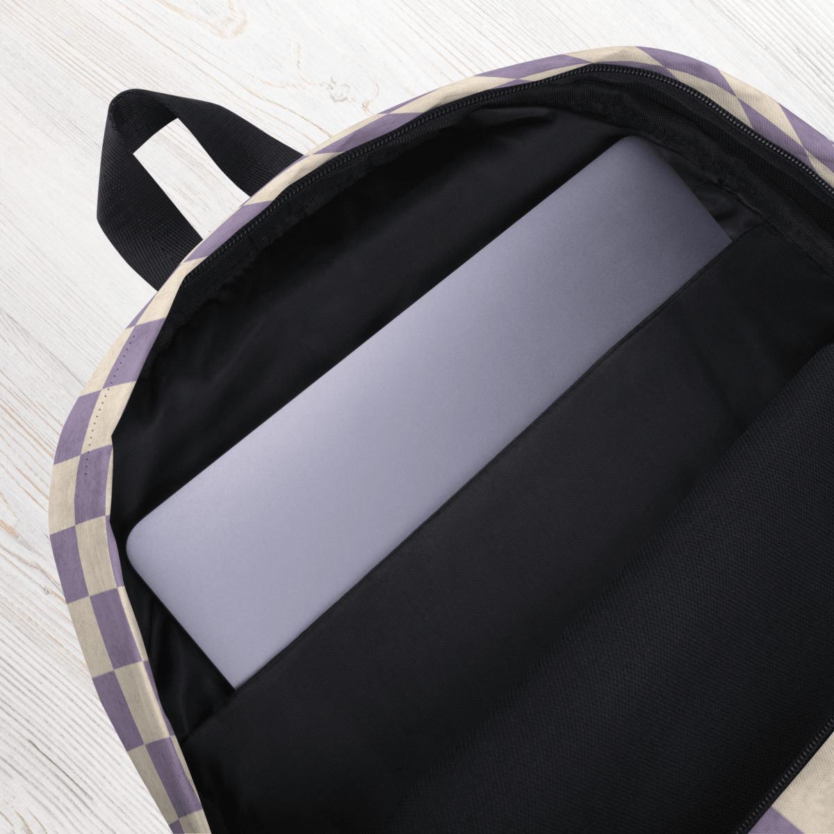 Backpack with a checkered pattern on the outside, containing a laptop on a light wooden surface.